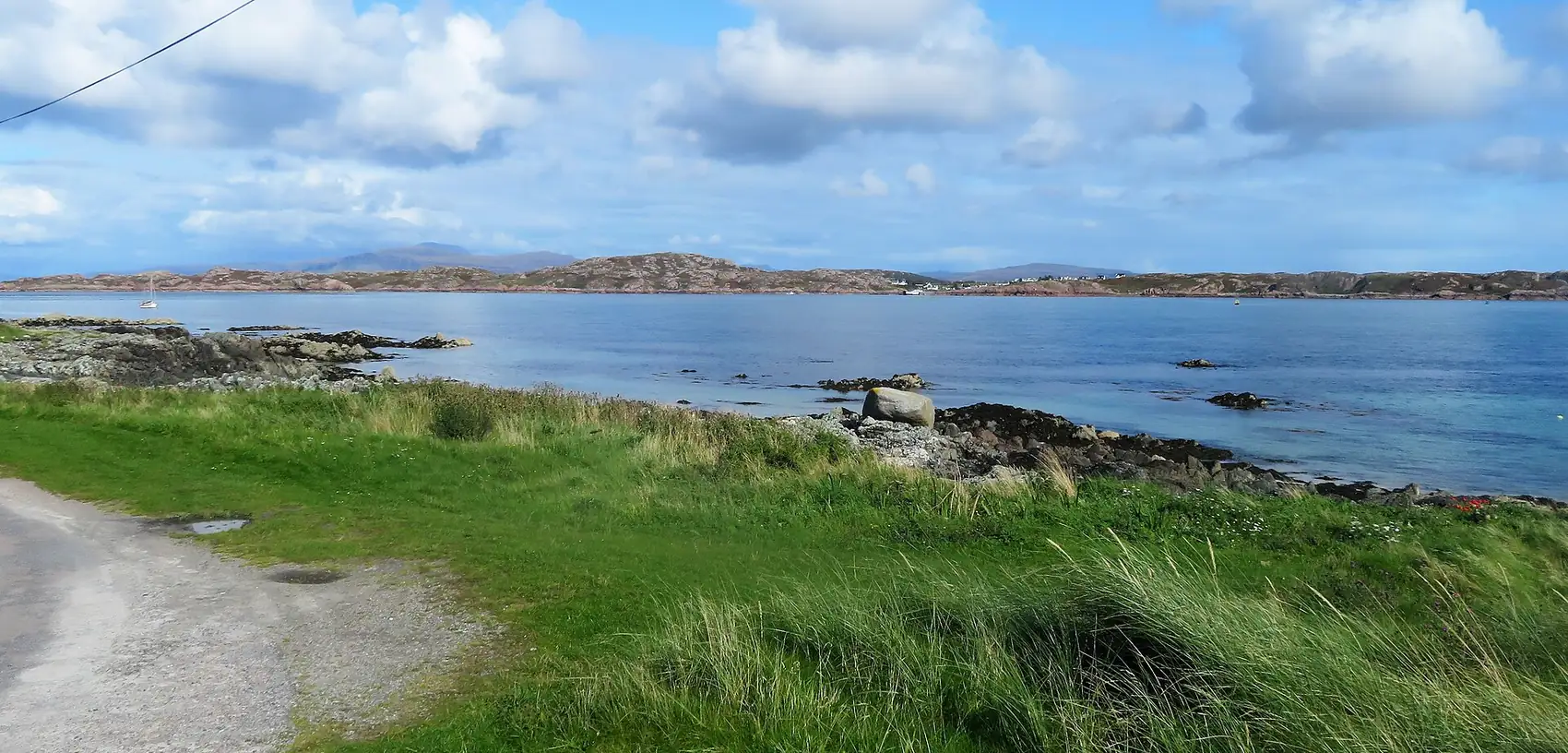 Il prato verde di Iona che scende verso il mare, sotto un cielo di nuvole